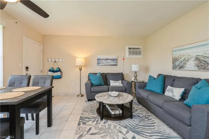 Tiled living room featuring a wall mounted AC and ceiling fan