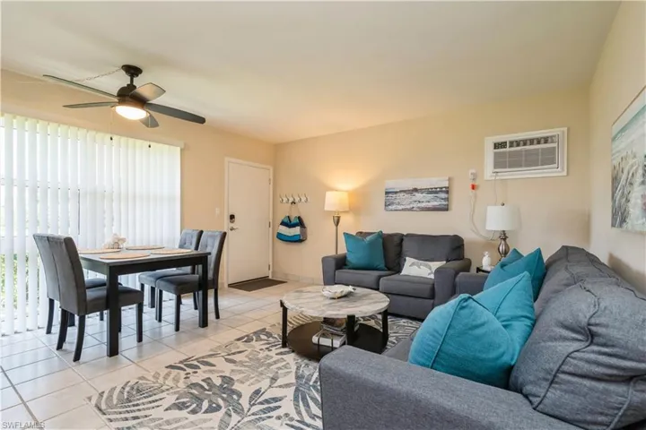 Living room with ceiling fan, light tile patterned floors, and an AC wall unit