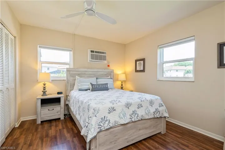 Bedroom featuring dark hardwood / wood-style flooring, a wall mounted air conditioner, ceiling fan, and a closet