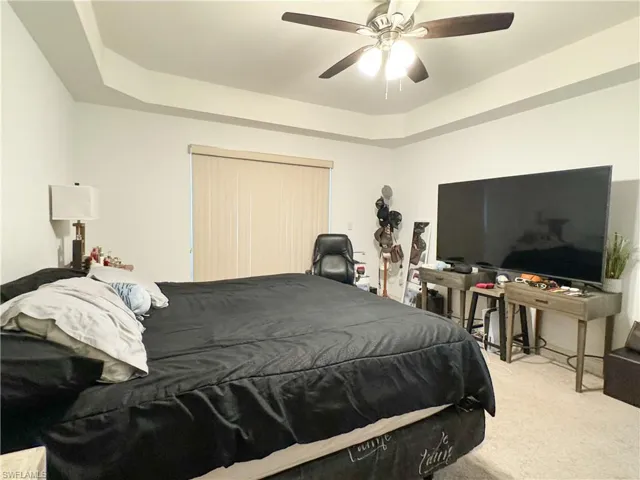 Bedroom with a tray ceiling, light colored carpet, and ceiling fan