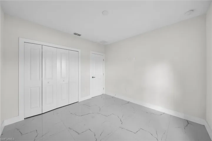 Spacious room featuring large format tile flooring with distinctive veining, white bi-fold closet doors, a neutral wall palette, recessed ceiling lighting, and crisp white trim
