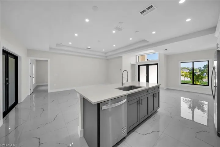 Spacious interior featuring large format tile flooring, recessed lighting, a kitchen island with an undermount sink, contemporary cabinetry, and stainless steel appliances