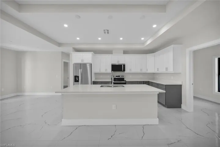 Modern kitchen featuring a large island, white shaker cabinetry, stainless steel appliances, and a marble-look tile floor