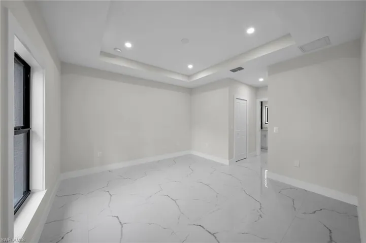 Spacious room featuring large format tile flooring, crown molding, a tray ceiling with recessed lighting, and a window with dark framing