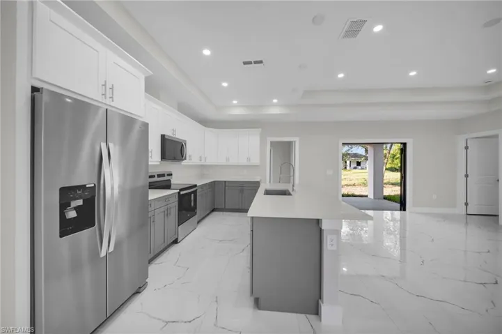 Kitchen featuring a two-tone cabinetry design, stainless steel appliances, a center island with a sink, quartz countertops, and recessed lighting