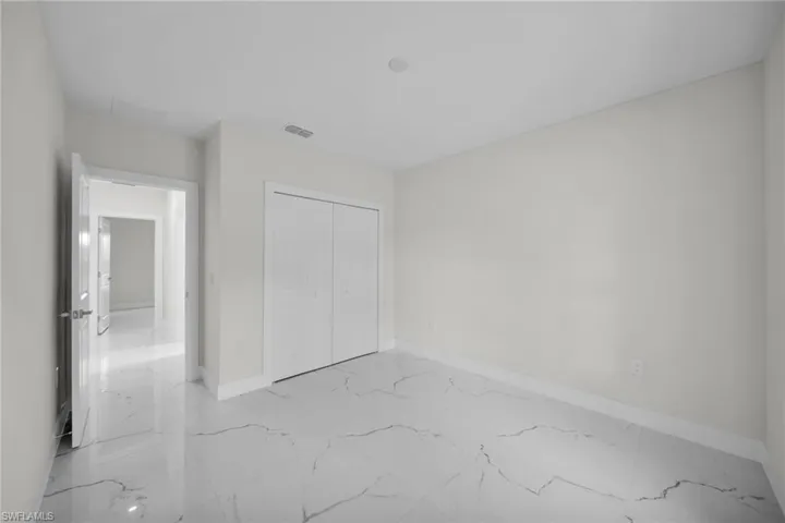 Spacious room featuring large format tile flooring with distinctive veining, a double bi-fold closet, a doorway with a modern lever handle, and neutral painted walls
