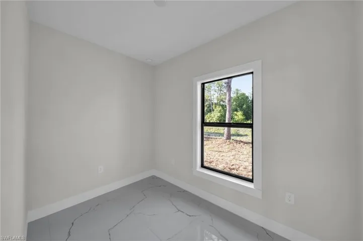 Interior room featuring light gray walls, a single-pane window with black trim and white casing, and gray tile flooring with white veining