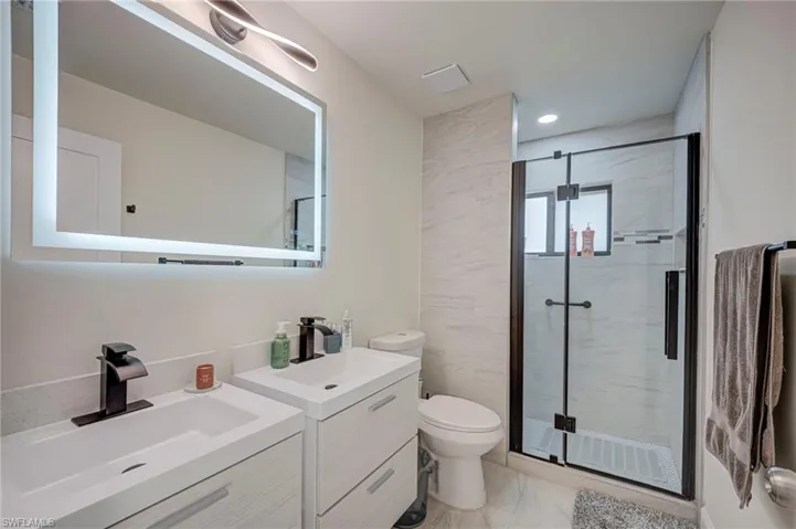 Bathroom featuring two vanities and a marble finish shower