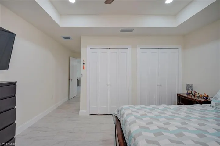 Bedroom featuring multiple closets, a raised ceiling, a ceiling fan, recessed lighting, and light marble finish floors