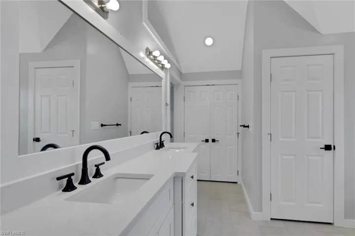 Full bathroom featuring double vanity, lofted ceiling, a closet, and light tile patterned floors