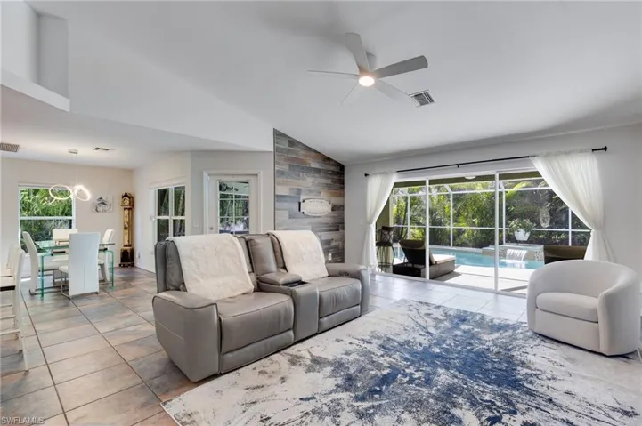 Living room with vaulted ceiling, light tile patterned flooring, a ceiling fan, and a sunroom