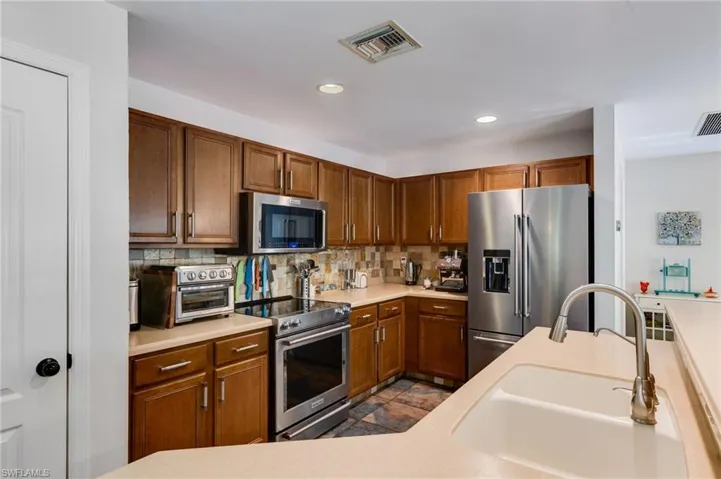 Kitchen featuring stainless steel appliances, light countertops, tasteful backsplash, recessed lighting, and brown cabinetry