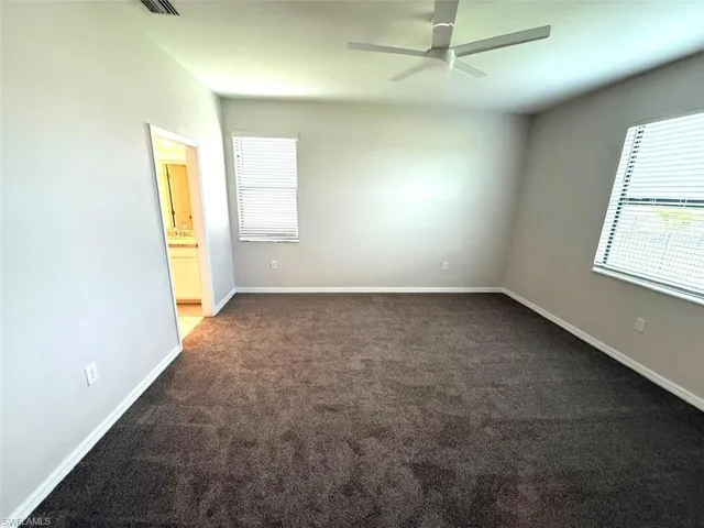 Unfurnished bedroom with multiple windows, dark colored carpet, a ceiling fan, and ensuite bathroom