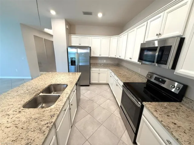 Kitchen with appliances with stainless steel finishes, light tile patterned floors, white cabinetry, light stone counters, and recessed lighting