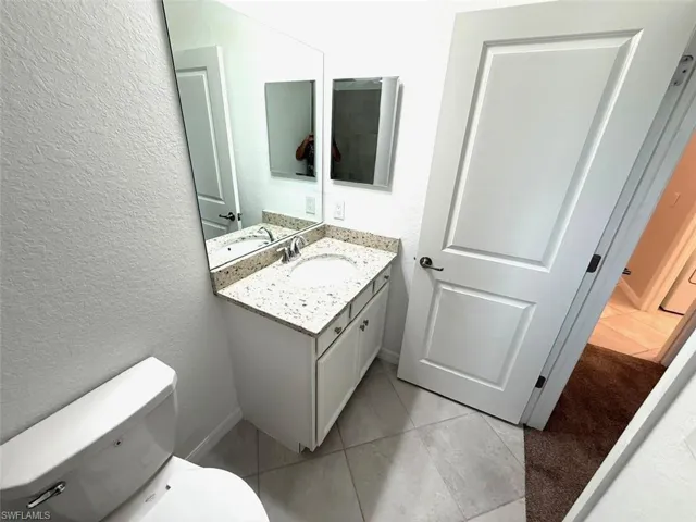 Half bathroom with vanity, a textured wall, and light tile patterned flooring