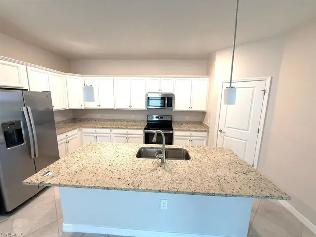 Kitchen featuring stainless steel appliances, light stone countertops, decorative light fixtures, white cabinetry, and light tile patterned flooring