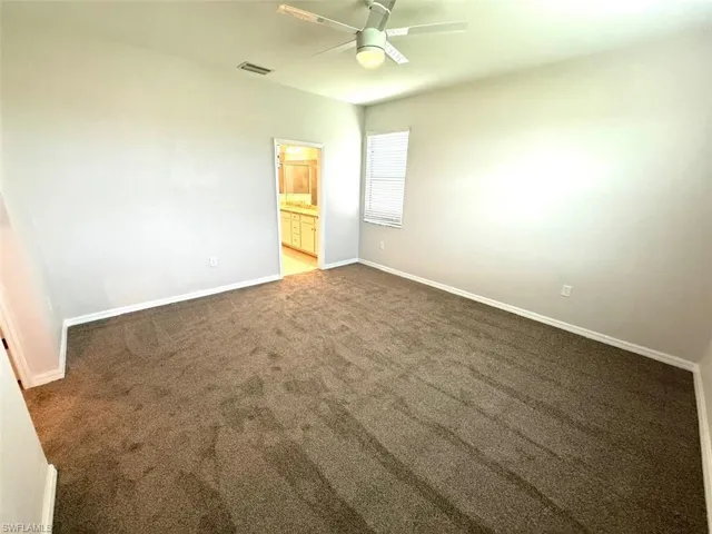 Unfurnished bedroom featuring connected bathroom, ceiling fan, and dark carpet