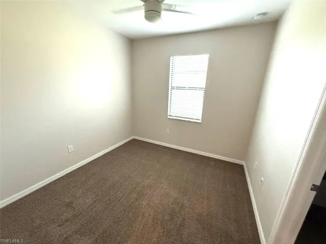 Unfurnished room featuring dark carpet and a ceiling fan