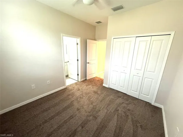 Unfurnished bedroom featuring dark colored carpet, a closet, and ceiling fan