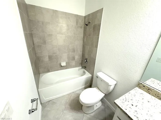 Bathroom featuring vanity, a textured wall, shower / tub combination, and tile patterned floors