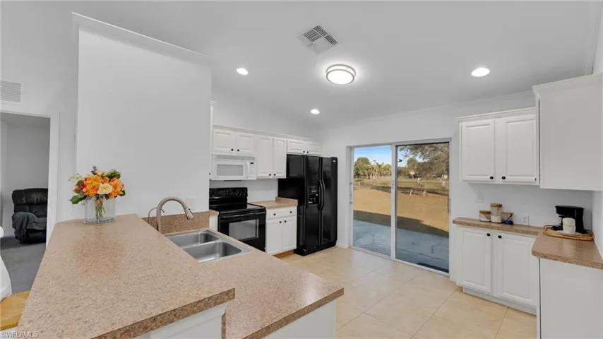 Kitchen with lofted ceiling, sink, black appliances, white cabinets, and kitchen peninsula