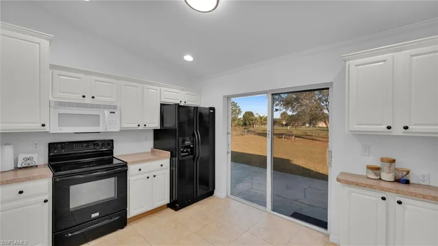 Kitchen featuring lofted ceiling, light tile patterned floors, ornamental molding, black appliances, and white cabinets