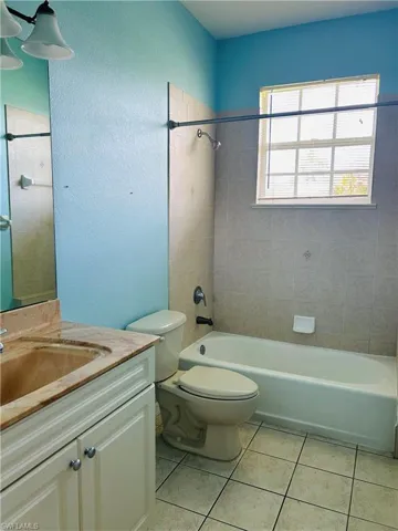 Full bath featuring vanity, bathtub / shower combination, light tile patterned floors, and a textured wall