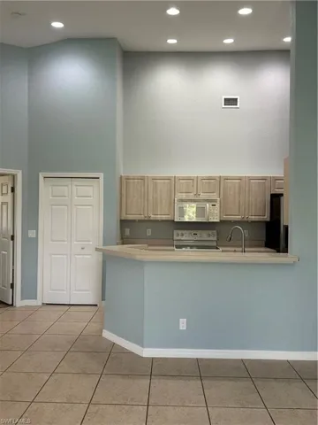 Kitchen featuring a high ceiling, light wood finish cabinetry, stove, a peninsula, and light tile patterned flooring