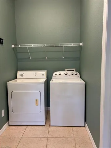 Laundry room with a textured wall, washer and clothes dryer, and light tile patterned floors