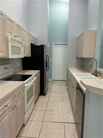 Kitchen featuring white range oven, light tile patterned flooring, light countertops, light wood finish cabinets, and a high ceiling