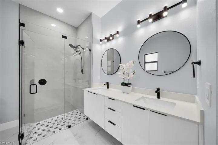 Full bathroom featuring double vanity, a stall shower, recessed lighting, and light marble finish flooring