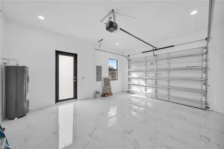 Garage with water heater, electric panel, recessed lighting, and a garage door opener