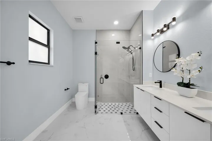 Full bathroom featuring double vanity, a shower stall, light marble finish floors, and recessed lighting
