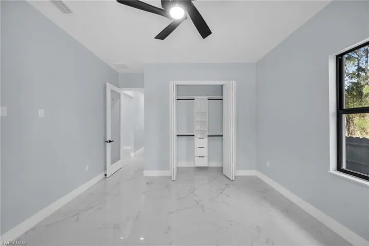 Unfurnished bedroom featuring multiple windows, a closet, ceiling fan, and light marble finish floors