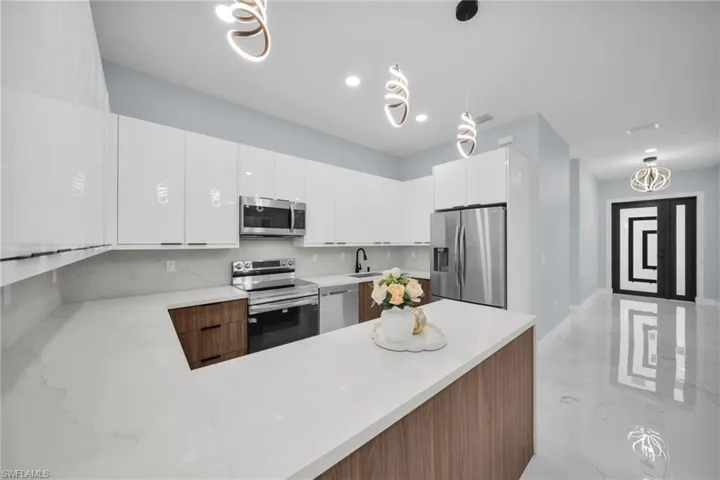 Kitchen featuring decorative light fixtures, stainless steel appliances, a peninsula, white cabinets, and modern cabinets