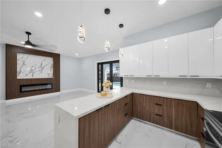 Kitchen featuring dual tone cabinets, a glass covered fireplace, a peninsula, modern cabinets, and decorative light fixtures