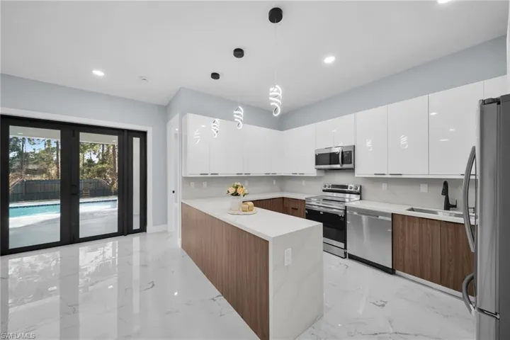 Dual tone kitchen with dual tone cabinets, stainless steel appliances, modern cabinets, light marble finish flooring, and pendant lighting