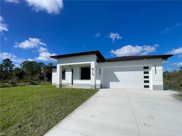 View of front facade with a front yard, a garage, driveway, stucco siding, and covered porch