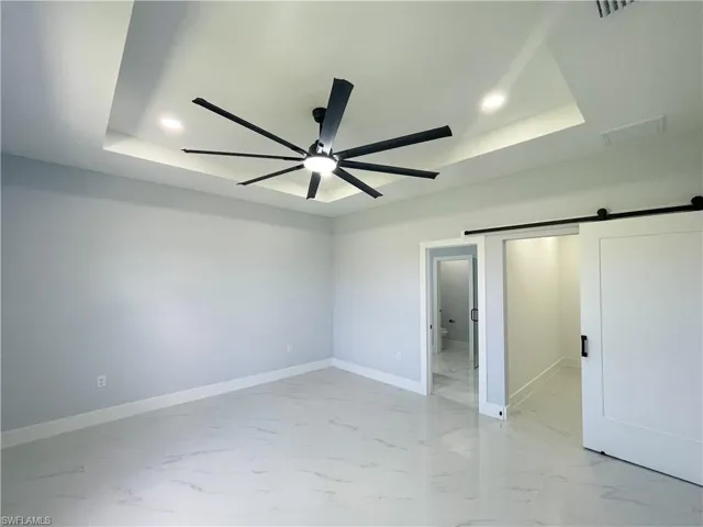 Unfurnished bedroom featuring a barn door, recessed lighting, light marble finish flooring, a ceiling fan, and a tray ceiling