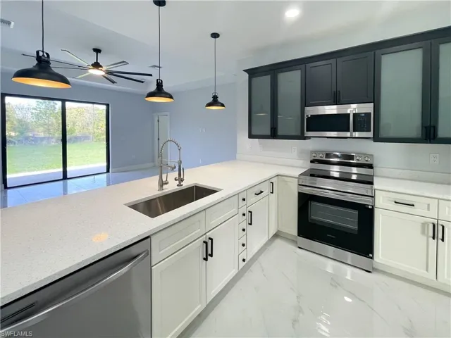 Kitchen featuring stainless steel appliances, light stone counters, decorative light fixtures, light marble finish floors, and glass insert cabinets