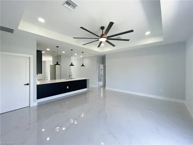 Unfurnished living room with ceiling fan, a tray ceiling, recessed lighting, and light marble finish flooring