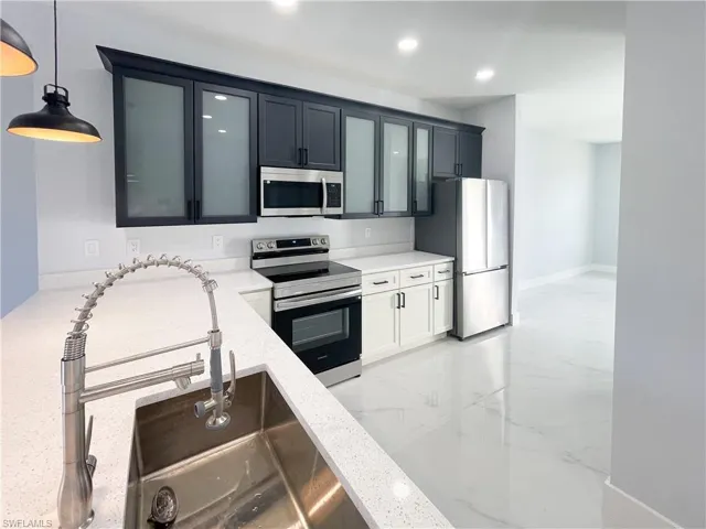 Kitchen with stainless steel appliances, glass insert cabinets, pendant lighting, and light stone counters