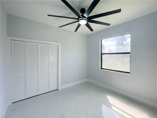 Unfurnished bedroom featuring light marble finish flooring, a closet, and a ceiling fan