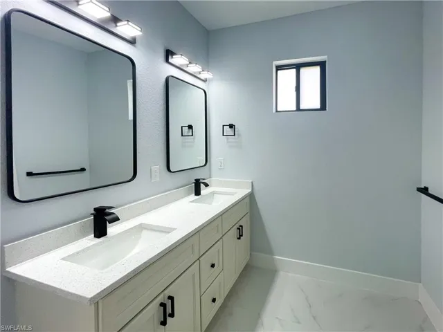 Bathroom with double vanity and light marble finish flooring