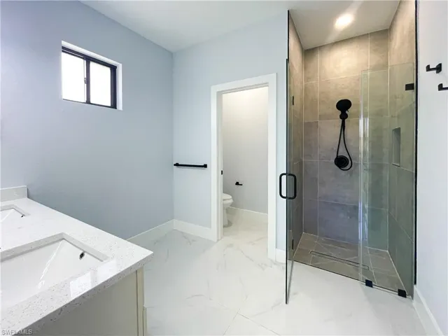 Bathroom with double vanity, a stall shower, and light marble finish floors