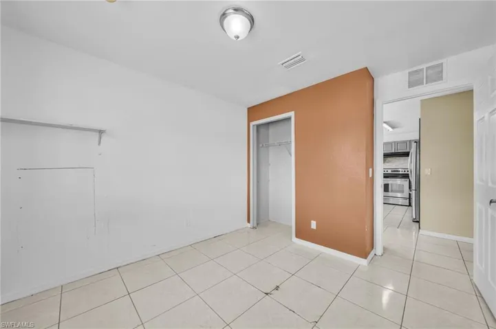 Unfurnished bedroom featuring light tile patterned floors, a closet, and freestanding refrigerator
