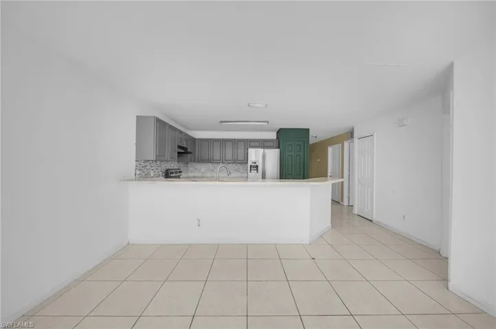 Kitchen featuring gray cabinets, a peninsula, stainless steel fridge with ice dispenser, light countertops, and decorative backsplash