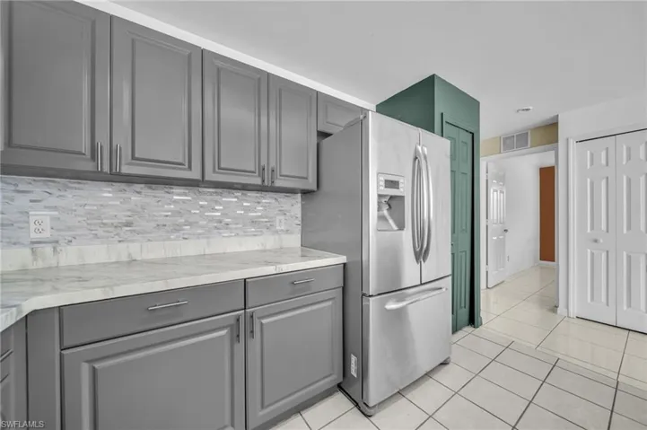Kitchen with light countertops, gray cabinets, stainless steel refrigerator with ice dispenser, and light tile patterned floors