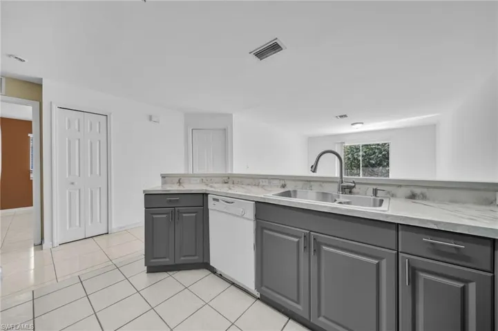 Kitchen with gray cabinetry, white dishwasher, light tile patterned floors, and light stone counters
