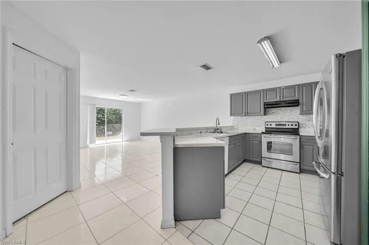 Kitchen featuring a peninsula, gray cabinetry, stainless steel appliances, light tile patterned floors, and light countertops